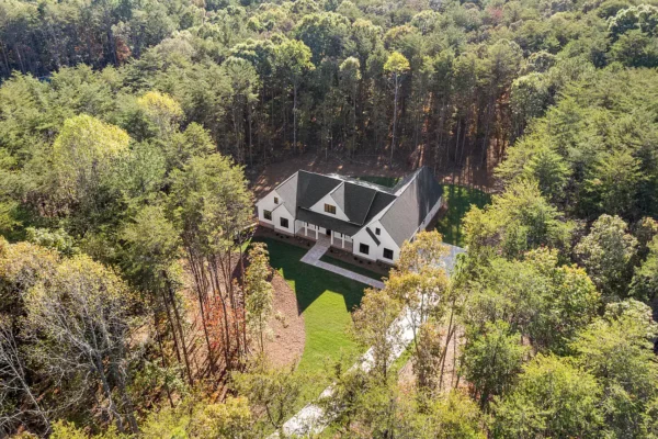 Modern farmhouse style home nestled in a wooded landscape with lush greenery and scenic surroundings.