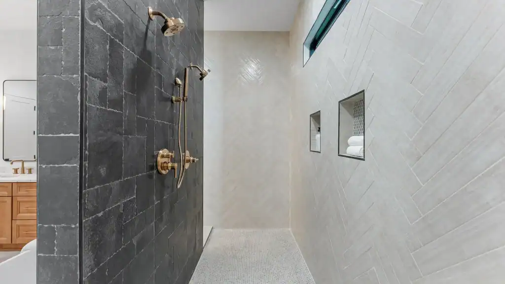 1ab9c64ed6247c1e4f7ee77392d1fa01-uncropped_scaled_within_1536_1152 Modern hotel-style walk-in shower with black slate tiles and brass fixtures, featuring built-in niches for toiletries.