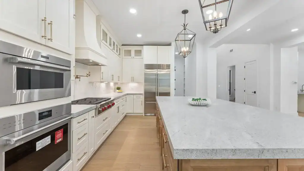 b9e6ef9728993963b0cae498123ab74d-uncropped_scaled_within_1536_1152 Modern white kitchen with marble island, stainless steel appliances, and elegant lighting.