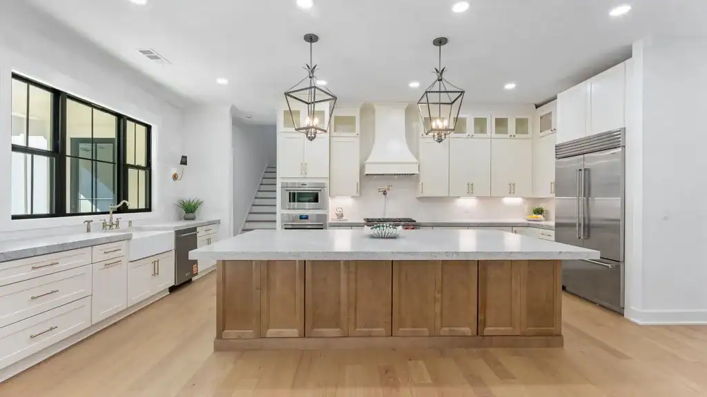 d256e6529c22f9be78aa0e78251db5e3-uncropped_scaled_within_1536_1152 Bright modern kitchen with white cabinetry, large island, stainless steel appliances, and elegant lighting fixtures.