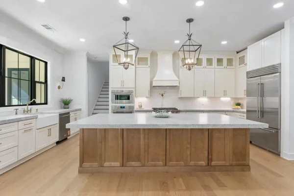 Bright modern kitchen with white cabinetry, large island, stainless steel appliances, and elegant lighting fixtures.