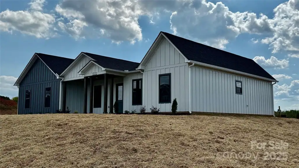 91f0d775cf04febd3fc88bdef28adb87-uncropped_scaled_within_1536_1152 Modern farmhouse-style new construction home with white and dark gray exterior siding, black window frames, under a partly cloudy sky.